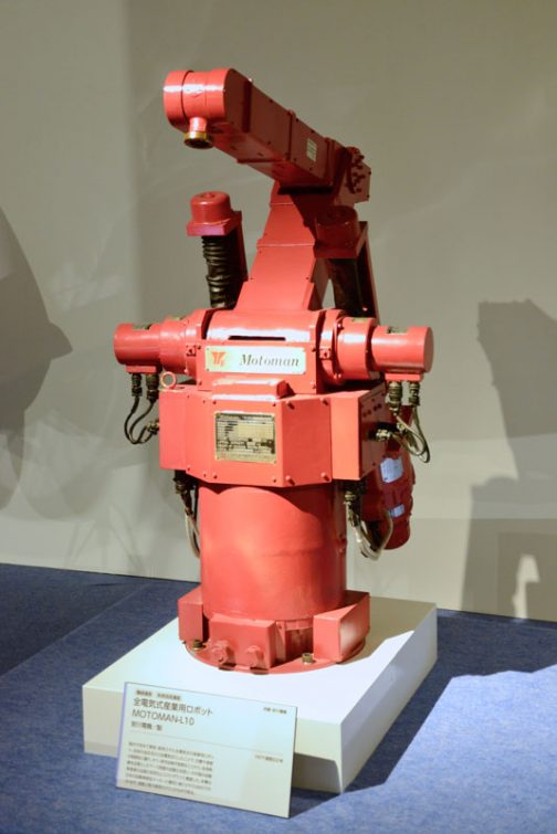 初期の頃の安川電機の産業用ロボット この展覧会のカタログの産業用ロボットのキャプションには 現代のモノづくりの場において、産業用ロボットの果たしている役割には、大きなものがあります。そのはじまりは1950年代。アメリカで概念が提唱され、ユニメート社によって、初めて実用化されました。日本においては川崎航空機工業が輸入・国産化し、国内でも産業用ロボットの開発が進みました。 　1970年代になると、産業用ロボットの研究も盛んになり、各社からいろいろなロボットが開発されるようになります。安川電機が1977（昭和52）年に国内で初めて開発・販売された全電気式の産業用ロボットは、従来の油圧式から全電気式にしたことで、位置や速度の制御製に優れ、かつ、保守点検が容易なことから、従来熟練を必要としたアーク溶接の自動化を担い、わが国の自動車産業の品質の安定化とコストダウンに貢献しました。こうしたロボットが日本の工業を発展させたのです。 とありました。