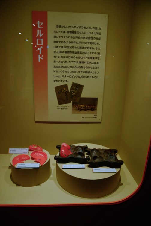 セルロイド 　昔懐かしいセルロイドのお人形、お面。セルロイドは、植物繊維のセルロースを化学処理して作られる世界初の熱可塑性の合成樹脂である。1868年にアメリカで発明され、日本では20世紀初めに製造が始まる。その後、日本の重要な輸出商品となり、1937（昭和12）年には日本のセルロイド生産量は世界一となった。かつては、筆箱や石けん箱、玩具など身の回りのいろいろな物がセルロイドでつくられていたが、今では高級メガネフレーム、ギターのピックなど限られたものに使われている。 とあります。 セルロイドがモーレツに燃えやすいの、知ってます。小さい頃ピンポン球を拾ってきて、細かく砕いて金属のエンピツキャップに詰め、口を叩いて潰してロケットを作ってました。ライターであぶるとすごい勢いで飛んで行くんです。行き先はコントロールできません。今考えると火事にならなくてよかった・・・