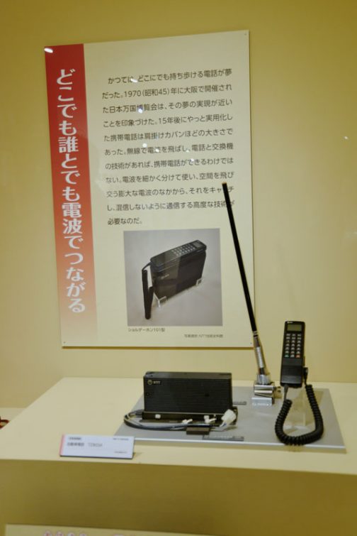 どこでも誰とでも電波でつながる かつてはどこにでも持ち歩ける電話が夢だった。1970（昭和45）年に大阪で開催された日本万国博覧会は、その夢の実現が近いことを印象づけた。15年後にやっと実現した携帯電話は肩掛けカバンほどの大きさであった。無線で電波を飛ばし、電話と交換機の技術があれば、携帯電話ができるわけではない。電波を細かく分けて使い、空間を飛び交う膨大な電波のなかから、それをキャッチし、混線しないように通信する高度な技術がひつようなのだ。 その下は自動車電話。そうそう！多くの人が見栄をはってインチキで付けていたのはこのアンテナです！